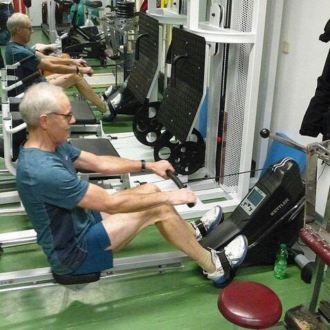 Mann im Fitnessstudio sitzt an einem Rudergerät und führt eine Ruderübung durch, im Hintergrund weitere Geräte sichtbar.