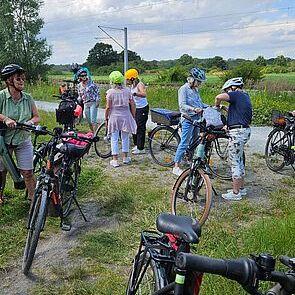Gruppe von Radfahrern in Helmen steht mit Fahrrädern auf einem Feldweg unter blauem Himmel und Wolken.