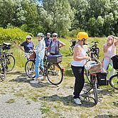 Gruppe von Radfahrern in Helm stehen mit Fahrrädern auf einem Weg in der Natur, umgeben von Grün.