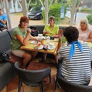 Vier Frauen sitzen in einem hellen Wintergarten an einem Tisch und genießen Kaffee und Snacks.