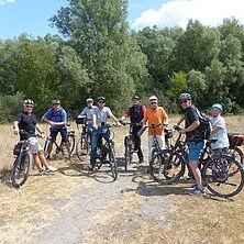 Gruppe von acht Radfahrern auf Fahrrädern in einem grünen Landschaftsbereich mit Bäumen im Hintergrund.