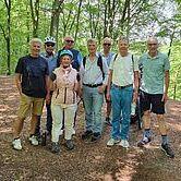 Gruppe von neun Personen in einem Wald, einige tragen Fahrräder, lächelnd auf einem schmalen Wanderweg.