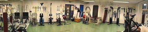 Fitnessraum mit verschiedenen Trainingsgeräten, darunter Fahrradergometer, Kraftmaschinen und eine Hantelbank.
