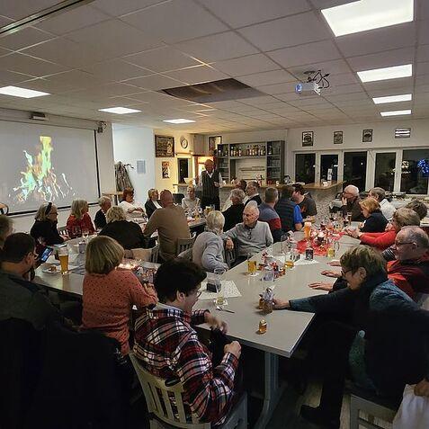 Gesellige Runde in einem Raum mit Tisch, Getränken und einer Projektion eines Kaminfeuers an der Wand.