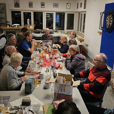 Geselliges Beisammensein am Tisch mit mehreren Personen, Geschenken und Getränken in einem hellen Raum.