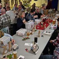 Weihnachtsfeier mit Gästen an einem Tisch, dekoriert mit Geschenken, Getränken und einer festlichen Atmosphäre.