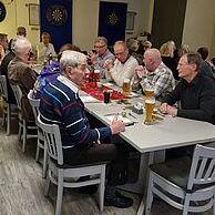 Gruppe älterer Männer sitzt an einem Tisch in einem Vereinsraum, Getränke und Essen sind auf dem Tisch verteilt.