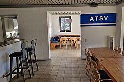 Blick in einen Vereinsraum mit Tischen, St&uuml;hlen und einer wandmontierten ATSV-Beschriftung.