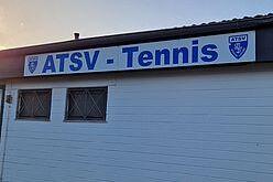 Signage des ATSV Tennis an einer wei&szlig;en Wand mit Fenstern im Hintergrund und Abendlicht.