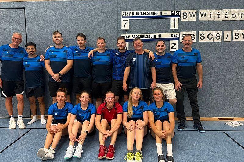 Gruppenfoto einer Tischtennismannschaft in blauen Trikots, zusammengesetzt aus Männern und Frauen, vor einem Punktestand.