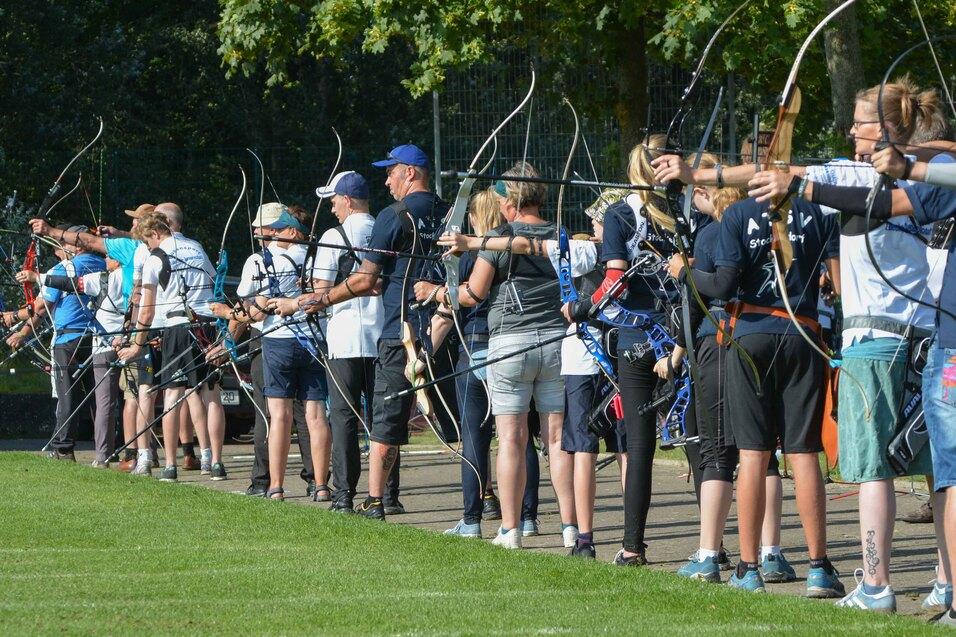Gruppe von Bogenschützen in einheitlicher Kleidung, die auf einem Feld mit Bögen und Pfeilen zielen.