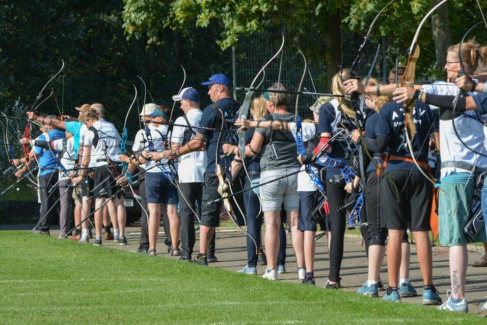 Gruppe von Bogenschützen in einheitlicher Kleidung, die auf einem Feld mit Bögen und Pfeilen zielen.