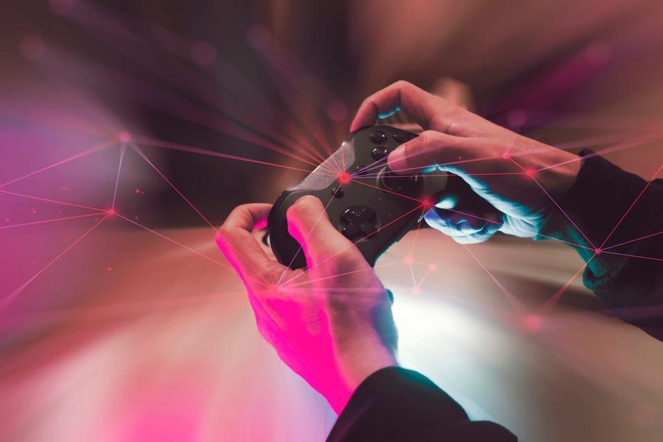 Hände halten einen Spielcontroller vor einem verschwommenen, bunten Hintergrund mit geometrischen Linien.