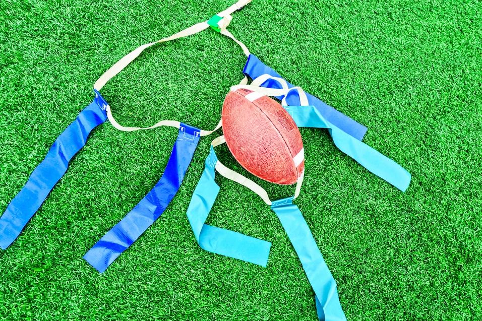 Rugbyball und Trainingswesten liegen auf grünem Kunstrasen.