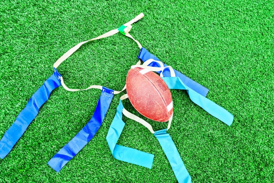 Rugbyball und Trainingswesten liegen auf grünem Kunstrasen.