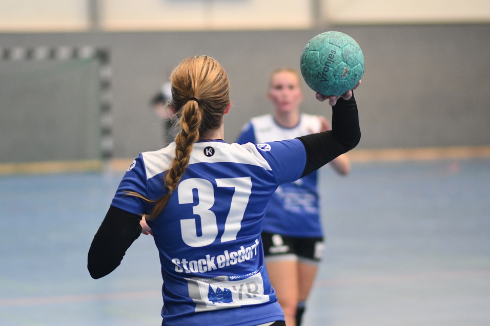 Handballspielerin mit der Nummer 37 hebt einen blauen Ball zur Abgabe eines Abwurfs in einer Sporthalle.