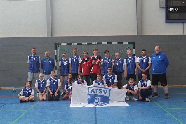 Gruppenfoto einer Handballmannschaft in blauen Trikots, die vor einem Tor mit einer ATSV-Flagge posiert.