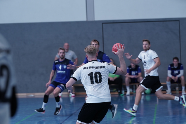 Spielszene eines Handballspiels: Spieler in wei&szlig; mit Ball, Gegner in blau im Hintergrund, Sporthalle.