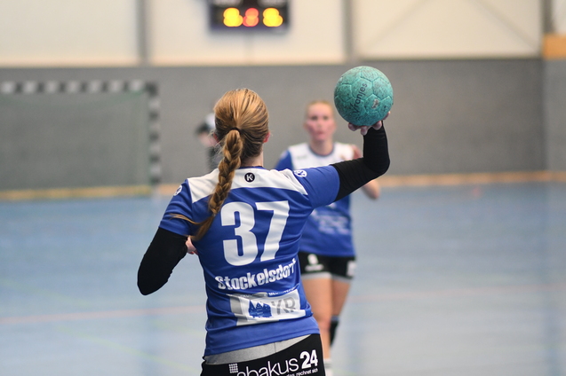 Handballspielerin mit der Nummer 37 hebt einen blauen Ball zur Abgabe eines Abwurfs in einer Sporthalle.