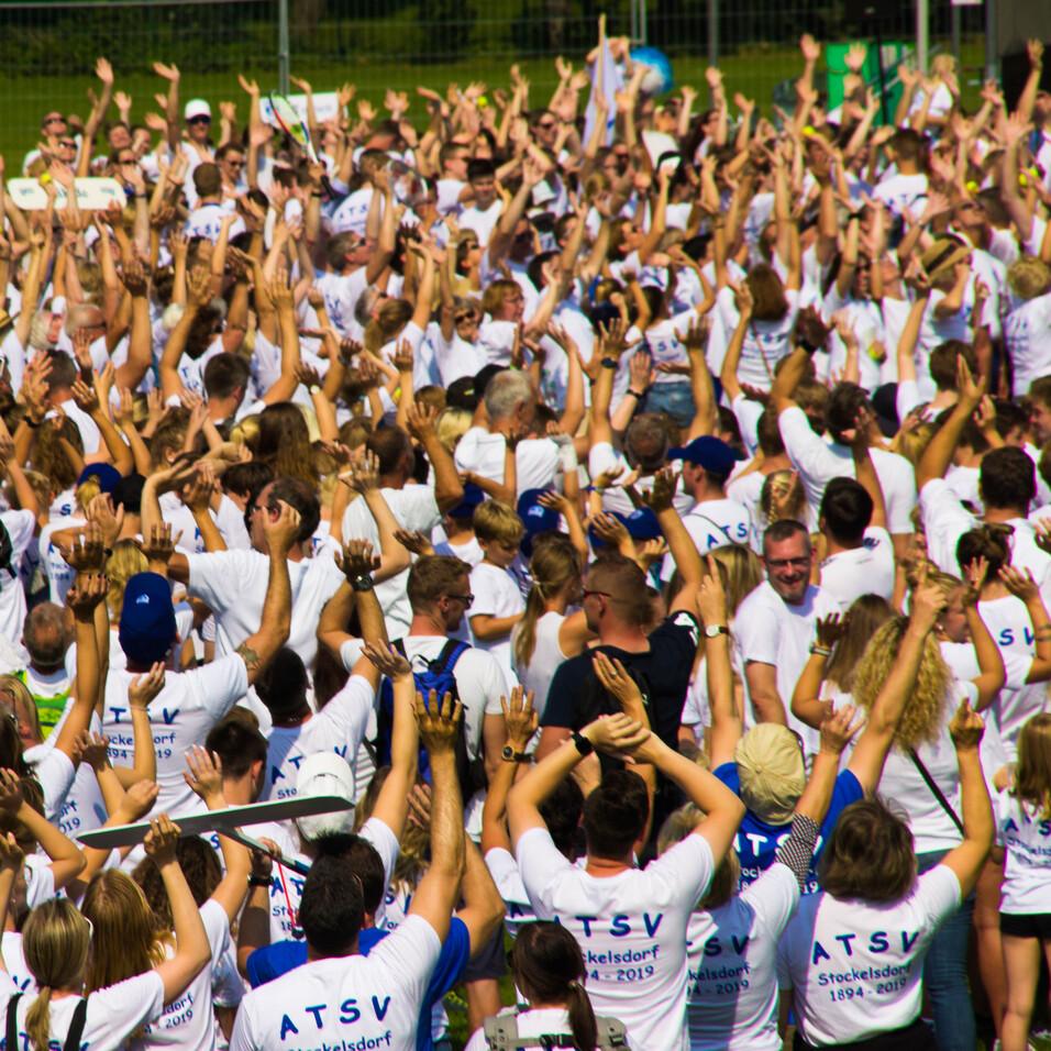 Gro&szlig;e Menschenmenge mit wei&szlig;en T-Shirts, die die H&auml;nde in die Luft heben, auf einem Freiluftgel&auml;nde.