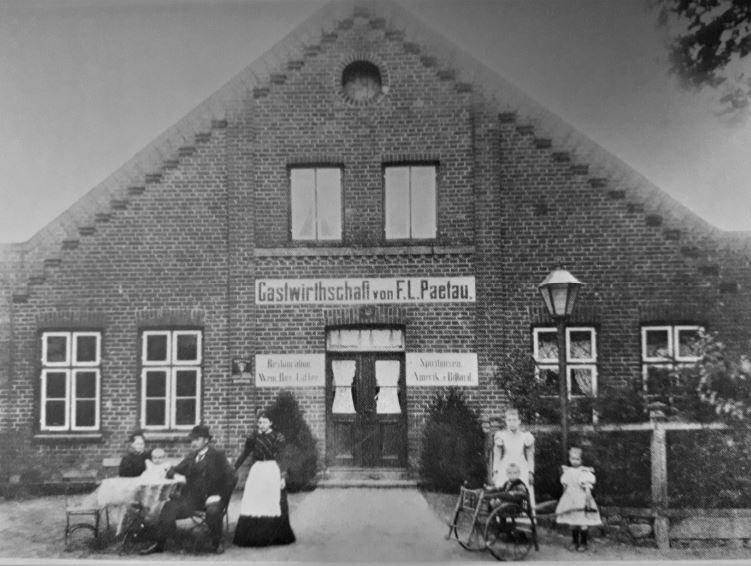 Historisches Gasthaus von F.L. Paetau mit G&auml;sten auf der Terrasse und zwei Kindern vor der Eingangst&uuml;r.