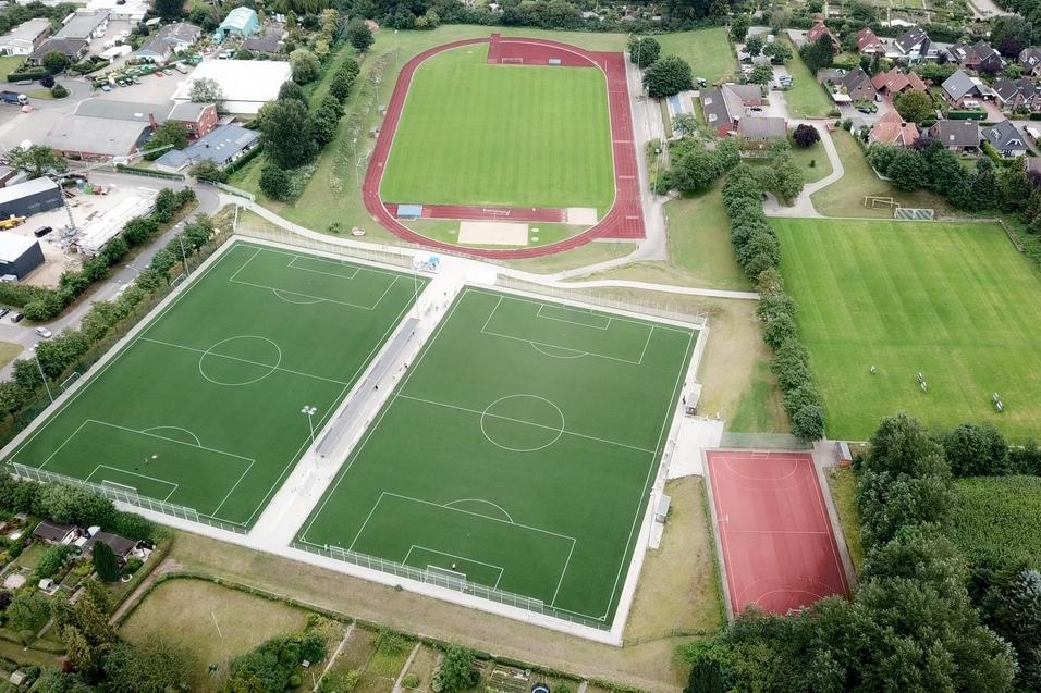 Luftaufnahme von Sportanlagen mit zwei Fu&szlig;ballfeldern, einer Laufbahn und einem Basketballplatz in einem gr&uuml;nen Umfeld.