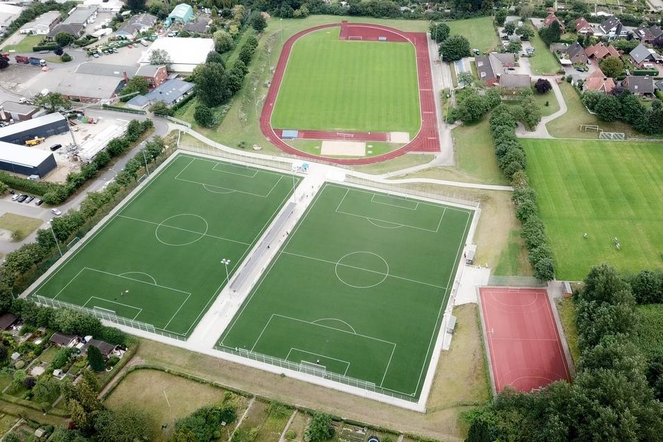 Luftaufnahme von Sportanlagen mit zwei Fu&szlig;ballfeldern, einer Laufbahn und einem Basketballplatz in einem gr&uuml;nen Umfeld.