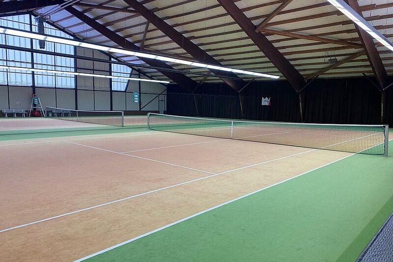 Innenansicht einer Tennishalle mit zwei Spielfeldnetzen und grüner sowie orangener Spielfeldmarkierung.