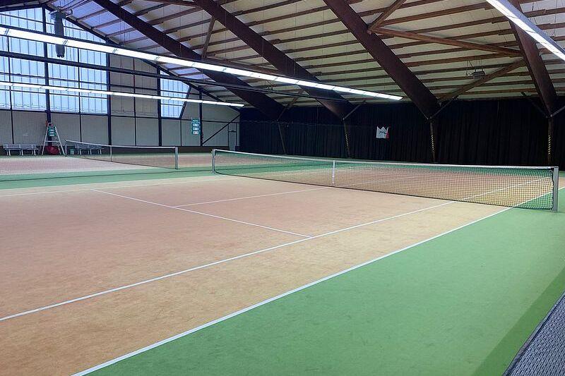 Innenansicht einer Tennishalle mit zwei Spielfeldnetzen und grüner sowie orangener Spielfeldmarkierung.