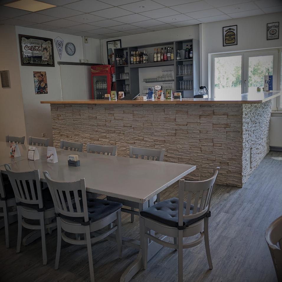 Innenansicht eines Caf&eacute;s mit einem steinernen Empfangstresen, St&uuml;hlen und Theke mit Getr&auml;nken im Hintergrund.